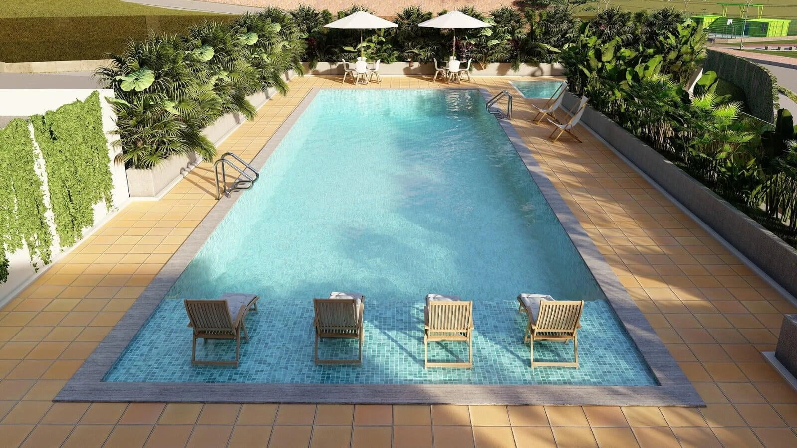 Aerial view of a rectangular swimming pool surrounded by loungers and lush green plants in a luxurious residential complex.