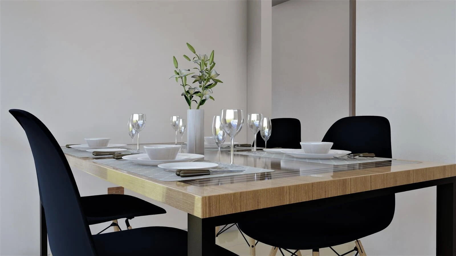 Elegant real estate visualization featuring a modern dining table set with black chairs, neatly arranged white dishes, and crystal wine glasses. A vase with fresh greenery adds a touch of nature to the sophisticated setup, complemented by the minimalist décor and soft lighting.